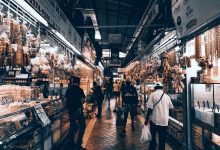Corredor movimentado de um mercado coberto, com lojas e pessoas fazendo compras.