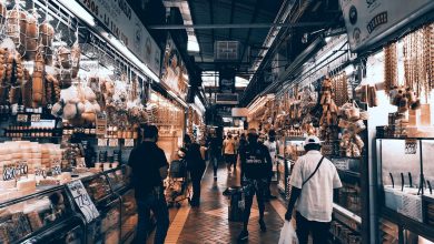 Corredor movimentado de um mercado coberto, com lojas e pessoas fazendo compras.