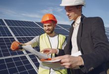 Engenheiro e empresário usando capacetes conversam sobre um projeto diante de uma instalação de energia solar