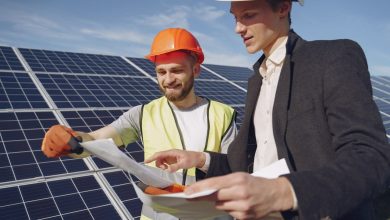 Engenheiro e empresário usando capacetes conversam sobre um projeto diante de uma instalação de energia solar