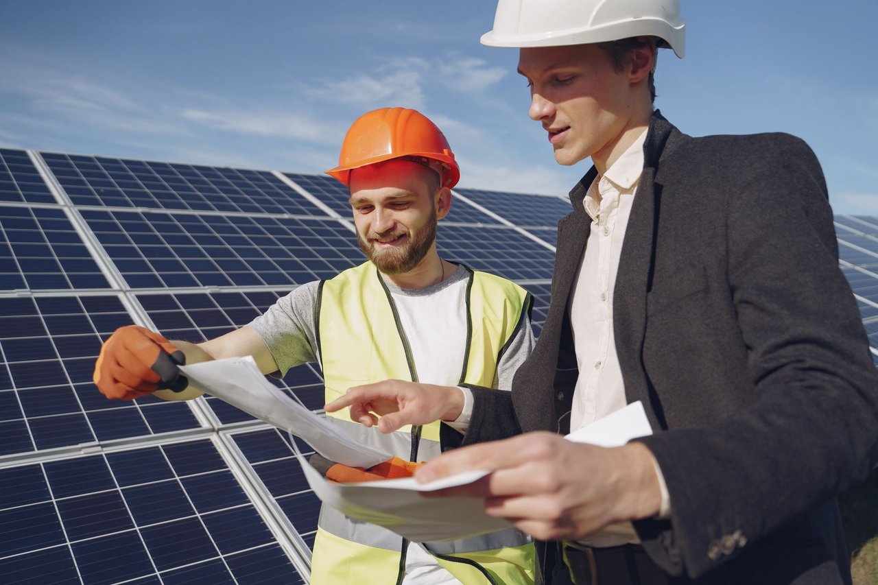 Engenheiro e empresário usando capacetes conversam sobre um projeto diante de uma instalação de energia solar