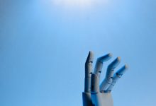 Mão robótica articulada estendida contra um fundo azul, em uma ilustração conceitual sobre inteligência artificial.