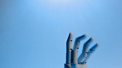 Mão robótica articulada estendida contra um fundo azul, em uma ilustração conceitual sobre inteligência artificial.