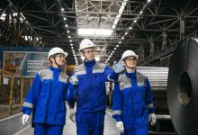 Trabalhadores usando equipamentos de segurança conversam dentro de uma fábrica siderúrgica.