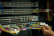 Mão organizando cabos de fibra óptica em uma sala de servidores.