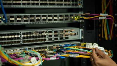 Mão organizando cabos de fibra óptica em uma sala de servidores.