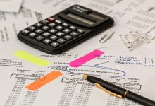 Calculadora, caneta e documentos sobre uma mesa de trabalho, representando análise financeira e contabilidade.