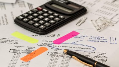 Calculadora, caneta e documentos sobre uma mesa de trabalho, representando análise financeira e contabilidade.