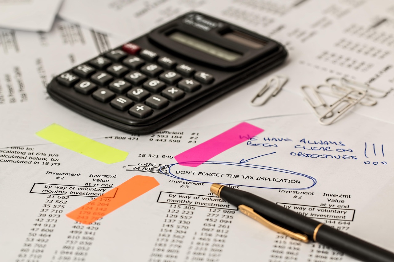 Calculadora, caneta e documentos sobre uma mesa de trabalho, representando análise financeira e contabilidade.